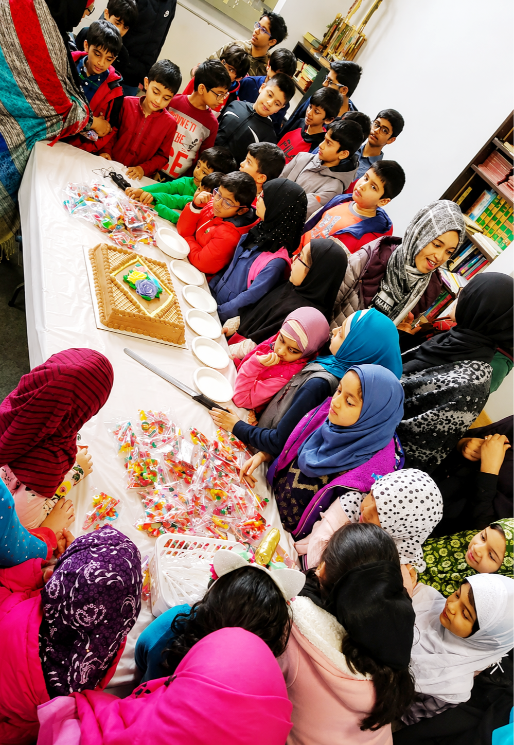 Students seated around a long table with a celebration cake and sweets