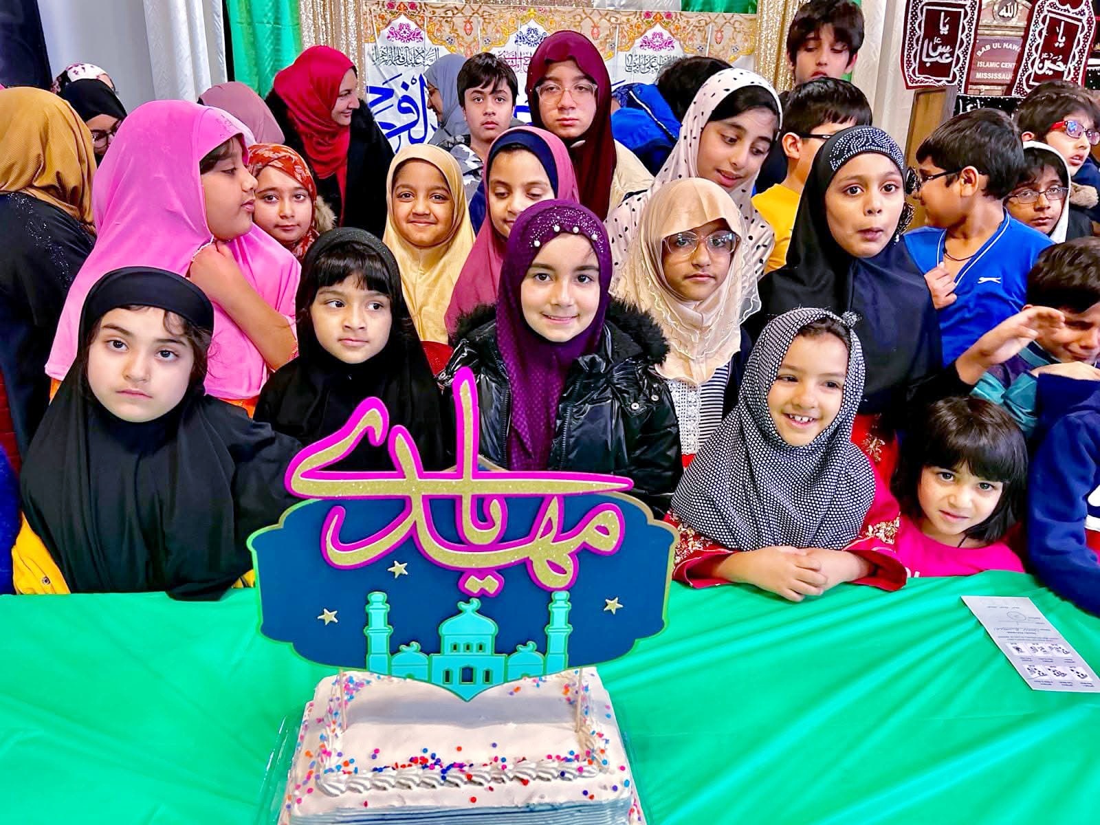 Zainabia Academy students gathered behind a Milad cake