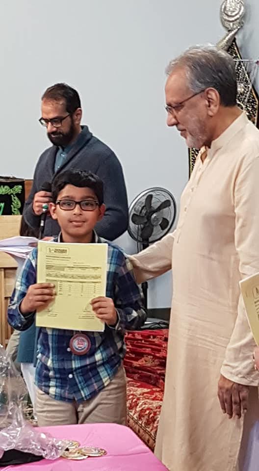 A student proudly holding up his Zainabia Academy report card