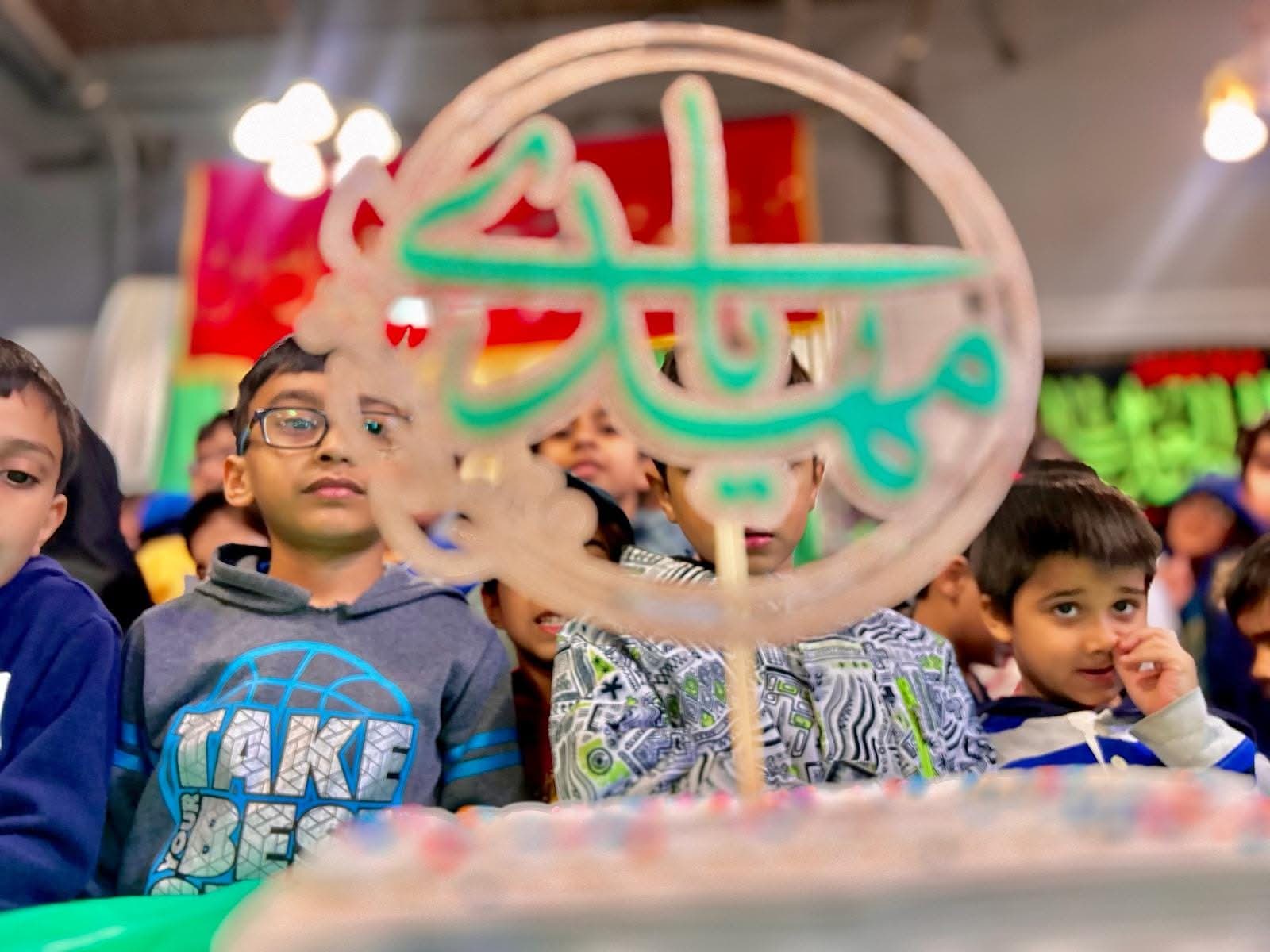 Students watching a Milad celebration behind a decorated cake